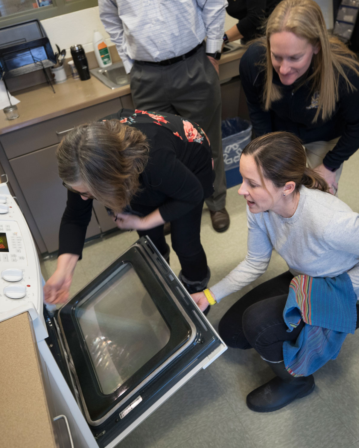 3 employees open an oven door and look inside to check on the food they made during a wellness event